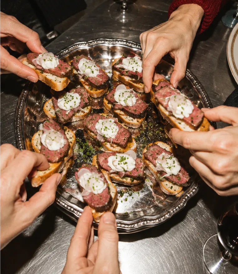 Hands reaching for steak canapés topped with cream on a silver serving tray
