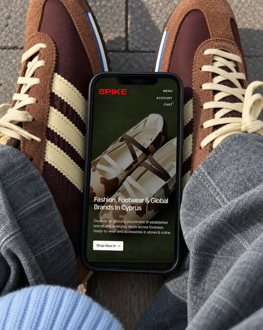 Spike sneaker shop shown on a phone held above a pair of trainers